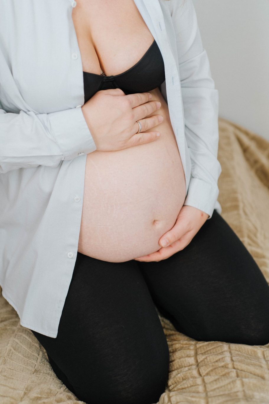 Femme enceinte en position assise, mains sur son ventre, vêtue d'une chemise ouverte.